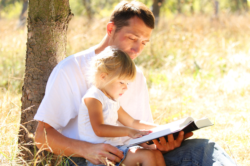 a young father with his little daughter reads the Bible